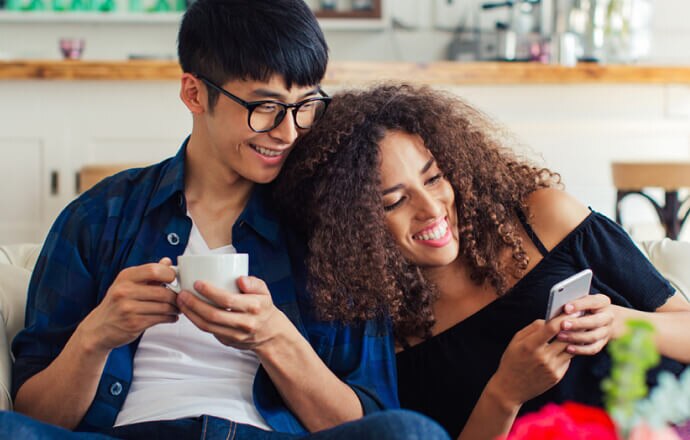 Hombre y mujer en el sofá miran el teléfono móvil protegido por Norton 360 for Mobile